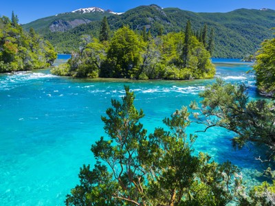 Azuurblauw meer met groene bossen en besneeuwde bergtoppen langs de Route Patagonië.