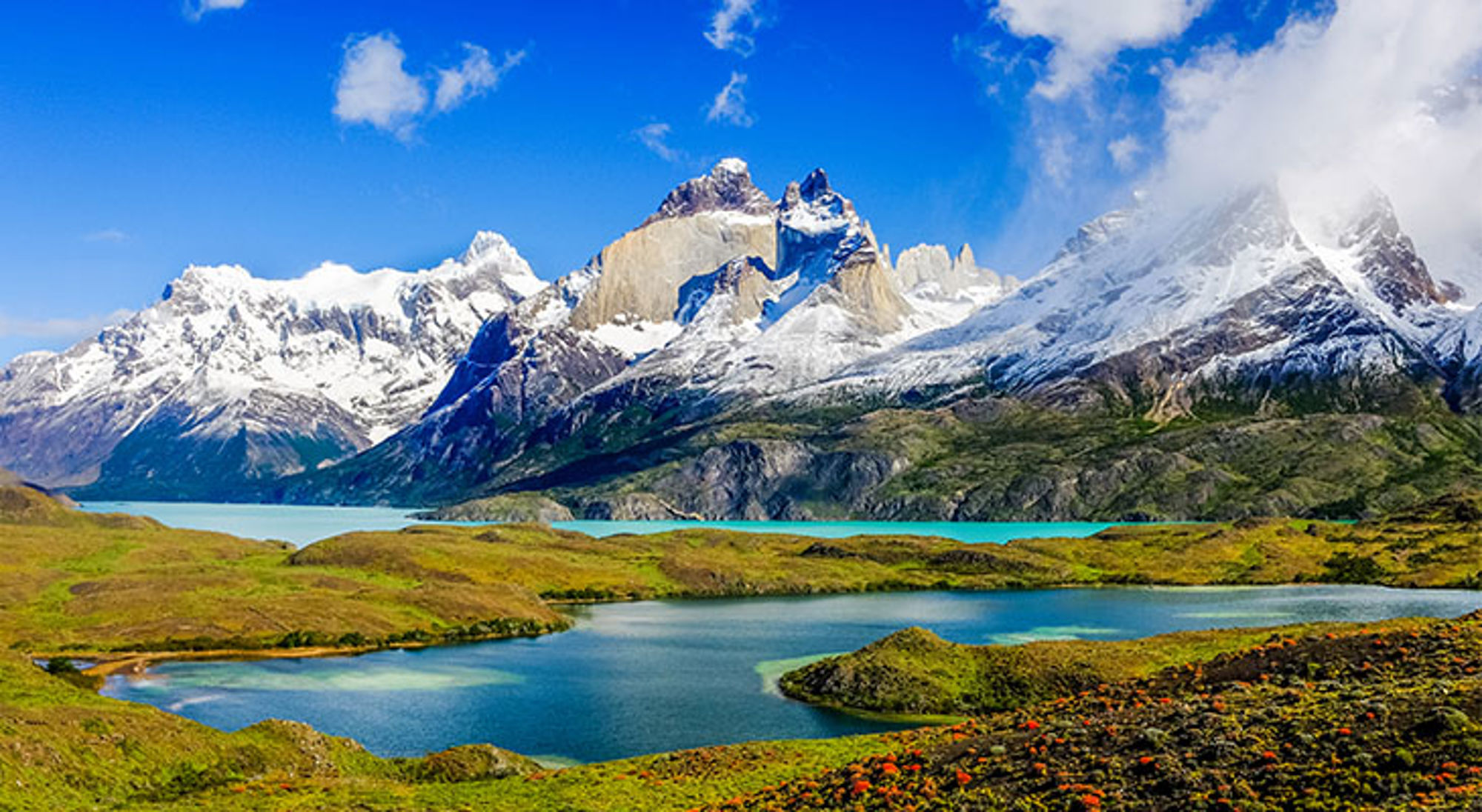 Besneeuwde bergtoppen en turquoise meren in Patagonië onder een heldere blauwe lucht.