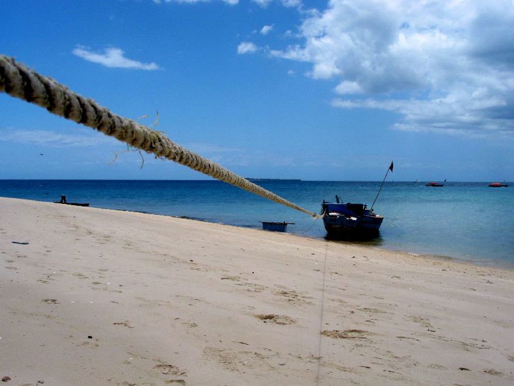 Houten boot aan een wit zandstrand bij helderblauw water tijdens groepsrondreis Zambia, Malawi en Tanzania.