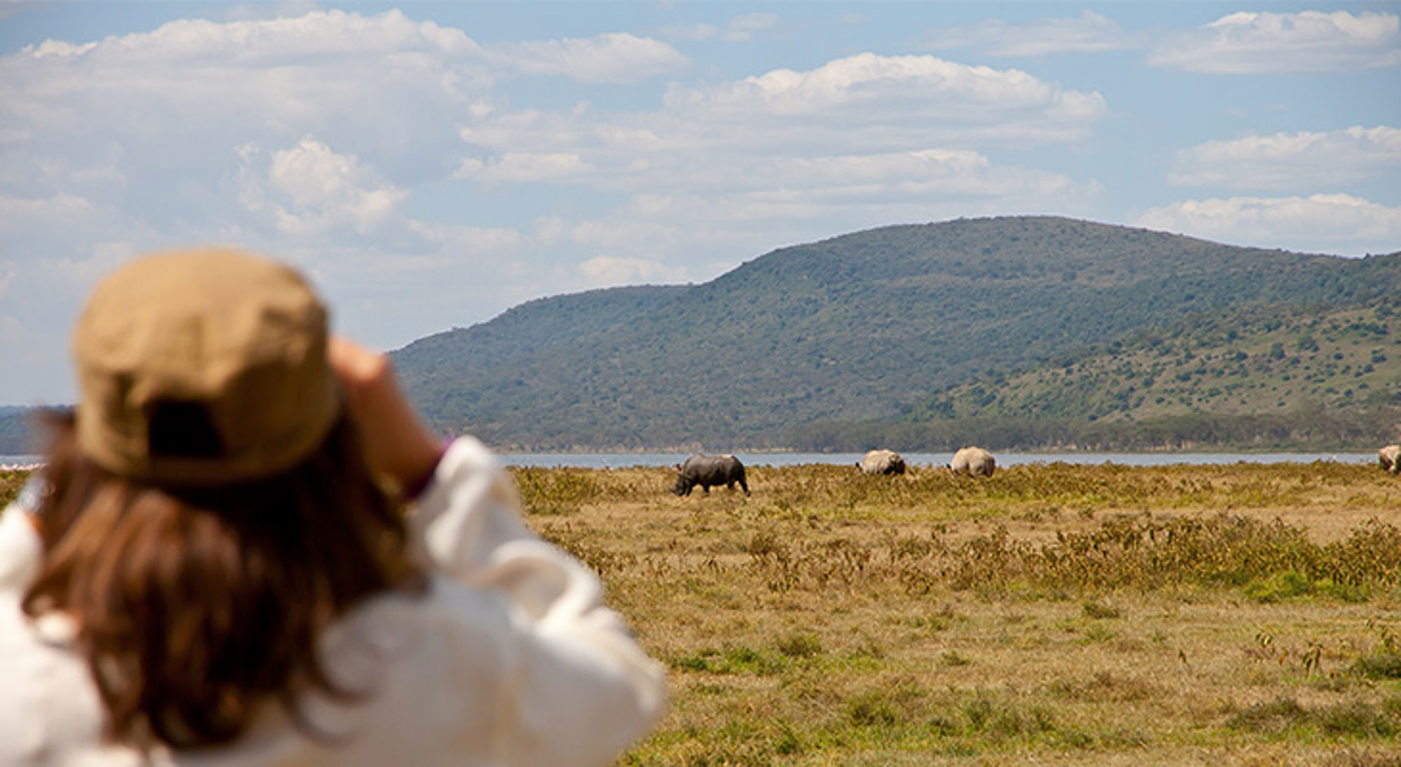 Toerist fotografeert neushoorns op de savanne in Kenia, met bergen op de achtergrond.