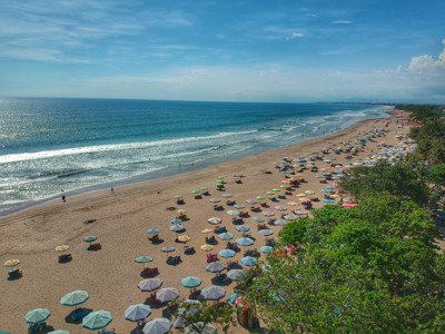 Overzicht van een lang zandstrand op Bali met kleurrijke parasols en golven langs de kust.