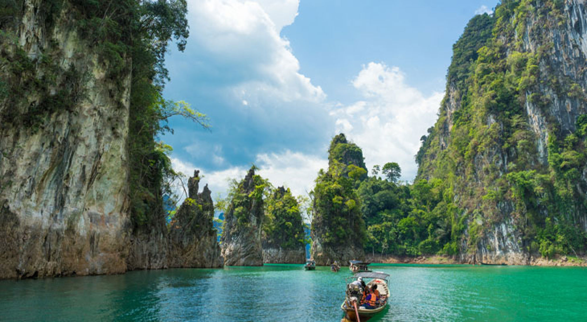 Boot op smaragdgroen water tussen kalkstenen kliffen in Khao Sok Nationaal Park, Thailand.