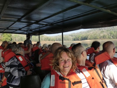 Reizigers met reddingsvesten tijdens een boottocht op een rivier in Zuid-India, met groene oevers op de achtergrond.