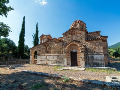 Byzantijnse stenen kerk op Evia, Griekenland, met cipressen en bergen onder een heldere blauwe lucht.