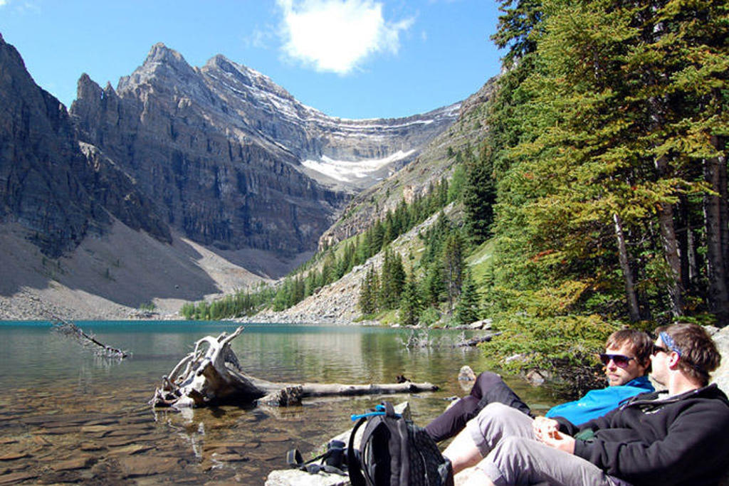 Twee reizigers ontspannen aan een bergmeer in de Canadese Rockies, met besneeuwde bergtoppen op de achtergrond.