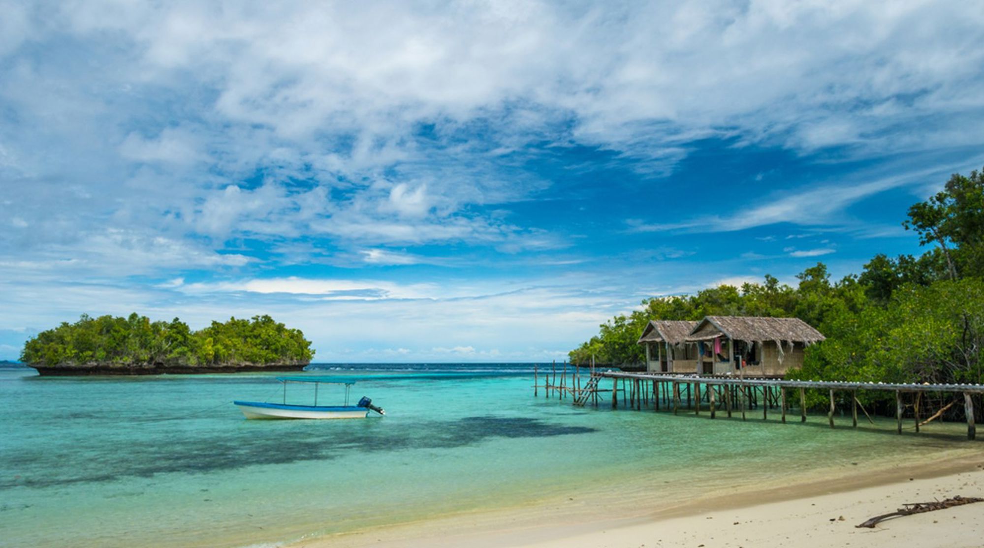 Houten paalwoning aan een tropische lagune met turquoise water en bootje in Indonesië.
