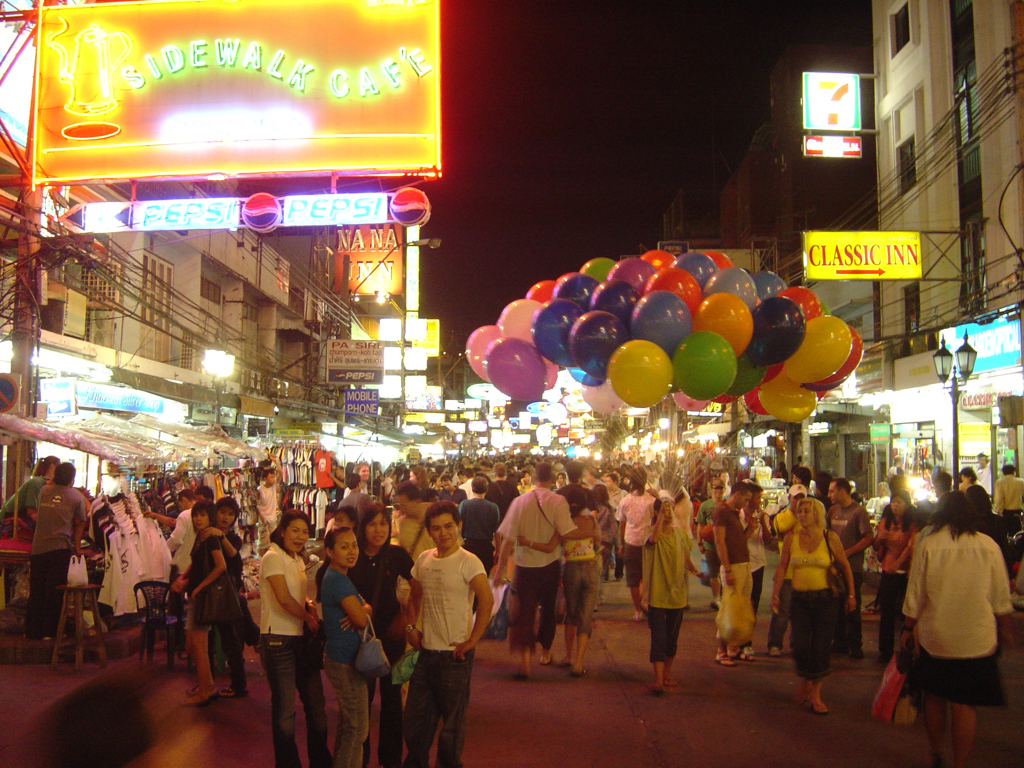 Avondmarkt in Bangkok met neonreclames, drukke straat en kleurrijke ballonnen.