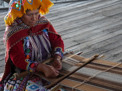 Vrouw in traditionele kleding weeft textiel op een houten weefgetouw in Peru.