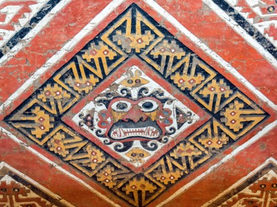 Detail van een kleurrijke muurschildering met mythisch gezicht in Chan Chan, Noord-Peru.