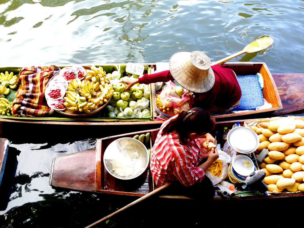 Drijvende markt in Thailand met boot vol tropisch fruit en twee verkopers op het water.