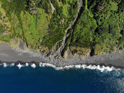 de ruige kust van São Miguel, Azoren, met zwarte rotsstrand en groen begroeide kliffen.