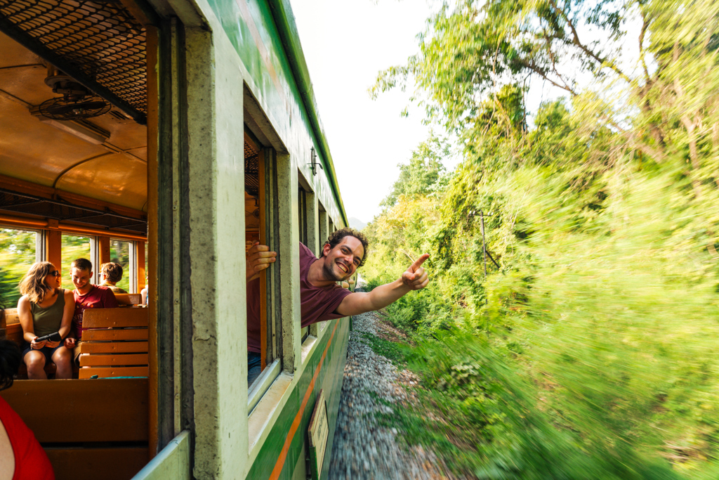 Reiziger leunt uit een rijdende trein tijdens een 22-35ers groepsrondreis door Thailand.