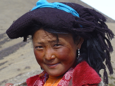 Portret van een meisje in Tibet met traditionele hoofdtooi en rode jas, tijdens de route Tibet en Nepal.