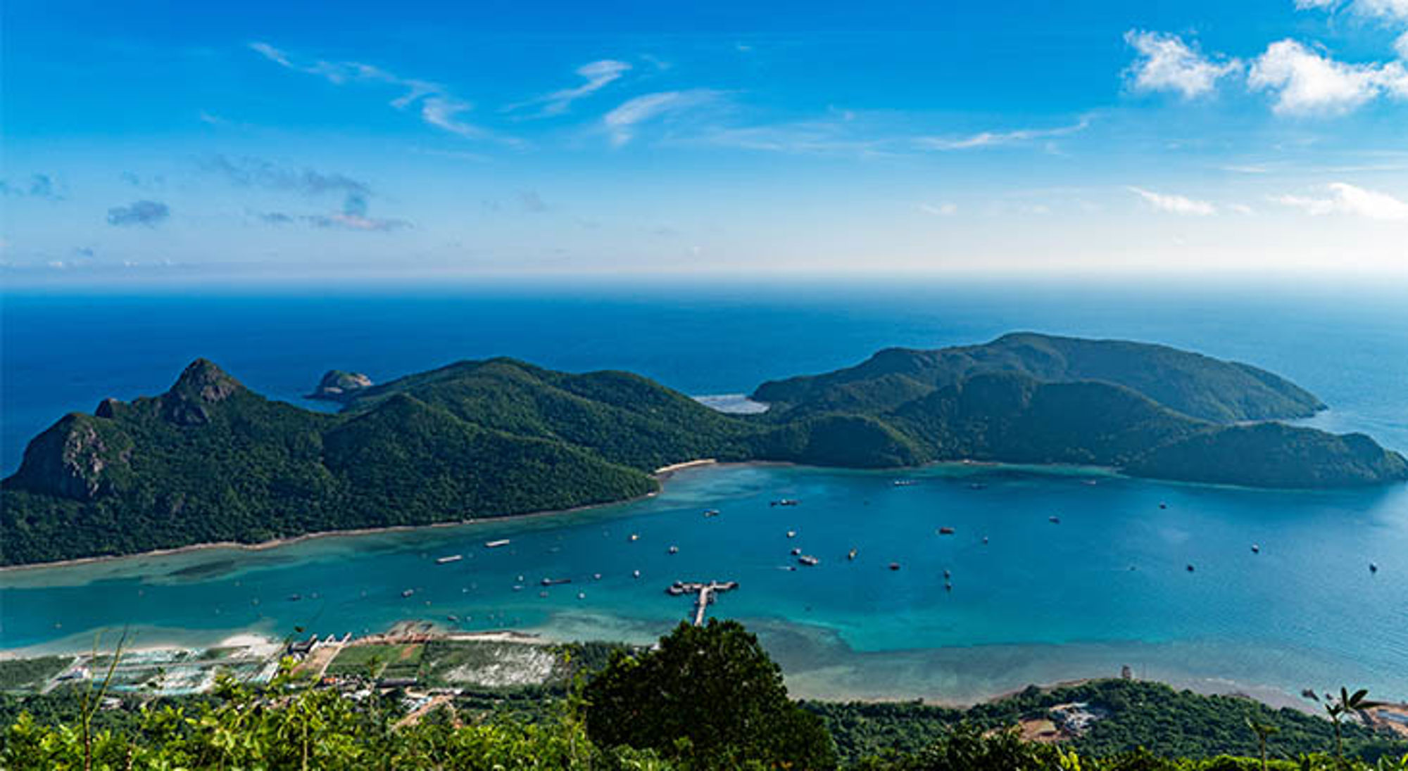 Panoramisch uitzicht op een baai met groene heuvels en turquoise zee met bootjes in Vietnam.