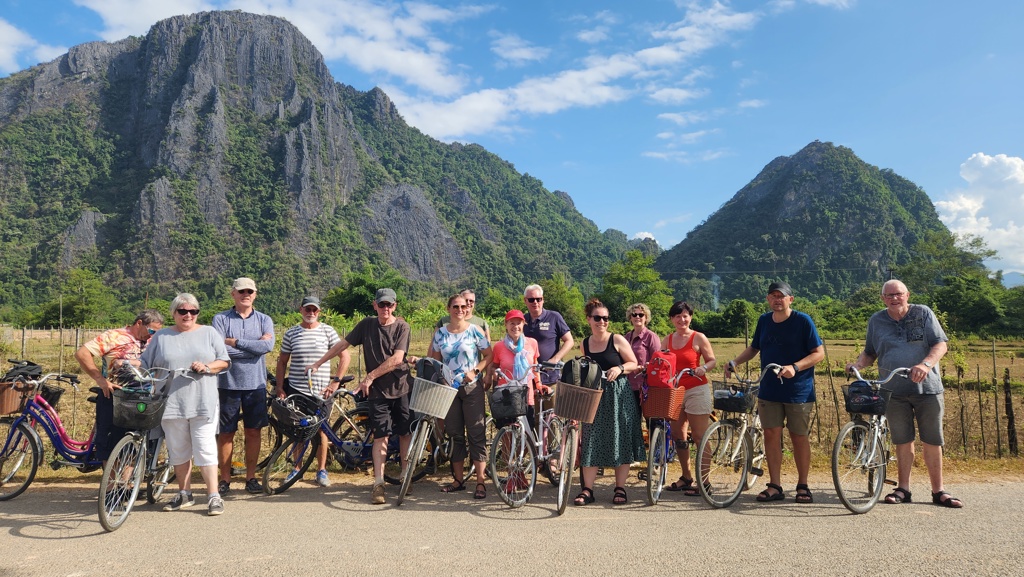Groepsrondreis Laos & Cambodja: reizigers met fietsen voor karstbergen in het groene landschap.