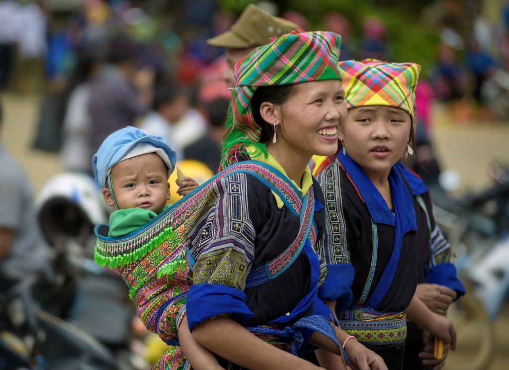 Vrouw in kleurrijke klederdracht met baby op de rug tijdens groepsrondreis Vietnam.