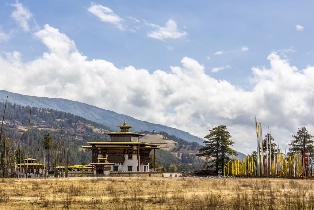 Traditioneel Bhutanese tempel in de Himalaya, omringd door gebedsvlaggen en bergen onder een blauwe lucht.