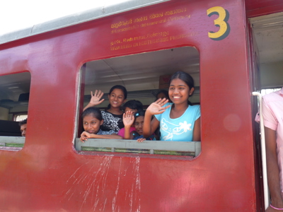Kinderen zwaaien vanuit een rode trein in Sri Lanka.