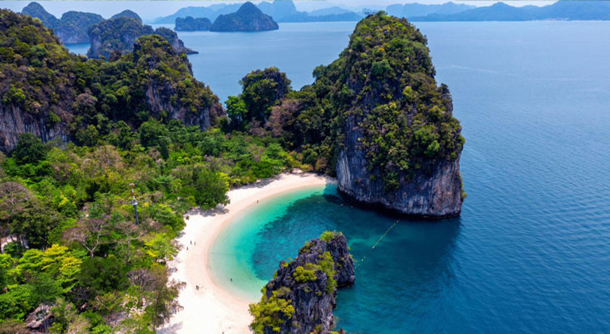 een wit zandstrand met turquoise zee en kalkstenen rotsen in Thailand.
