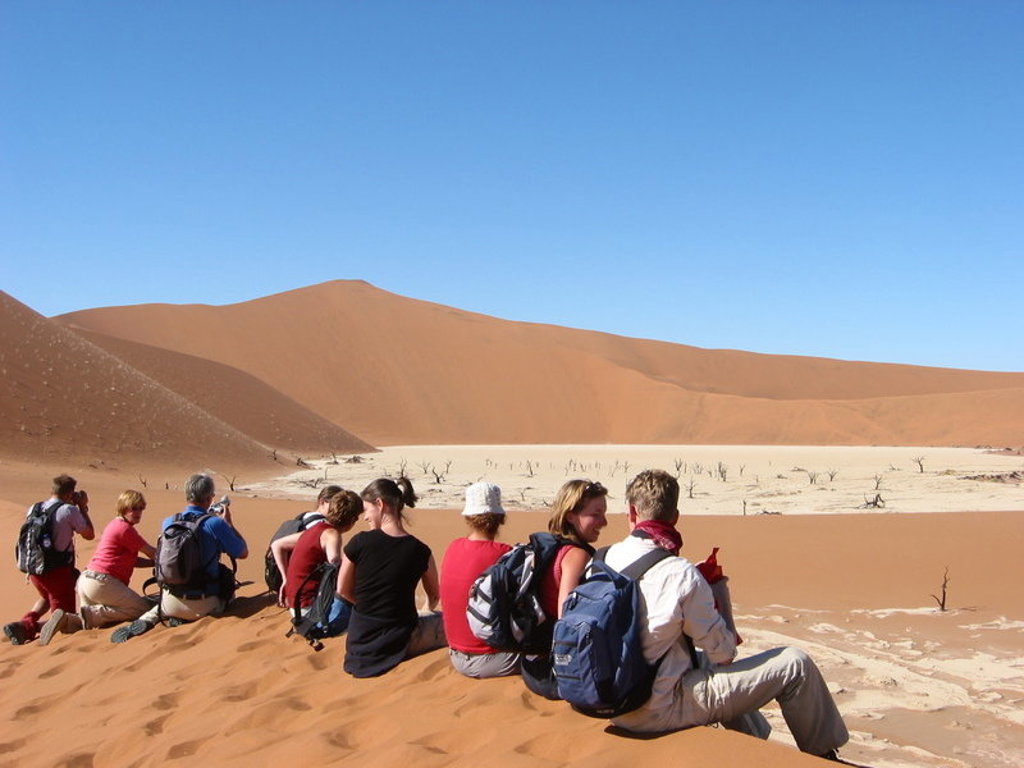 Groepsrondreis Namibië: reizigers rusten op een zandduin met uitzicht op Deadvlei en rode duinen.