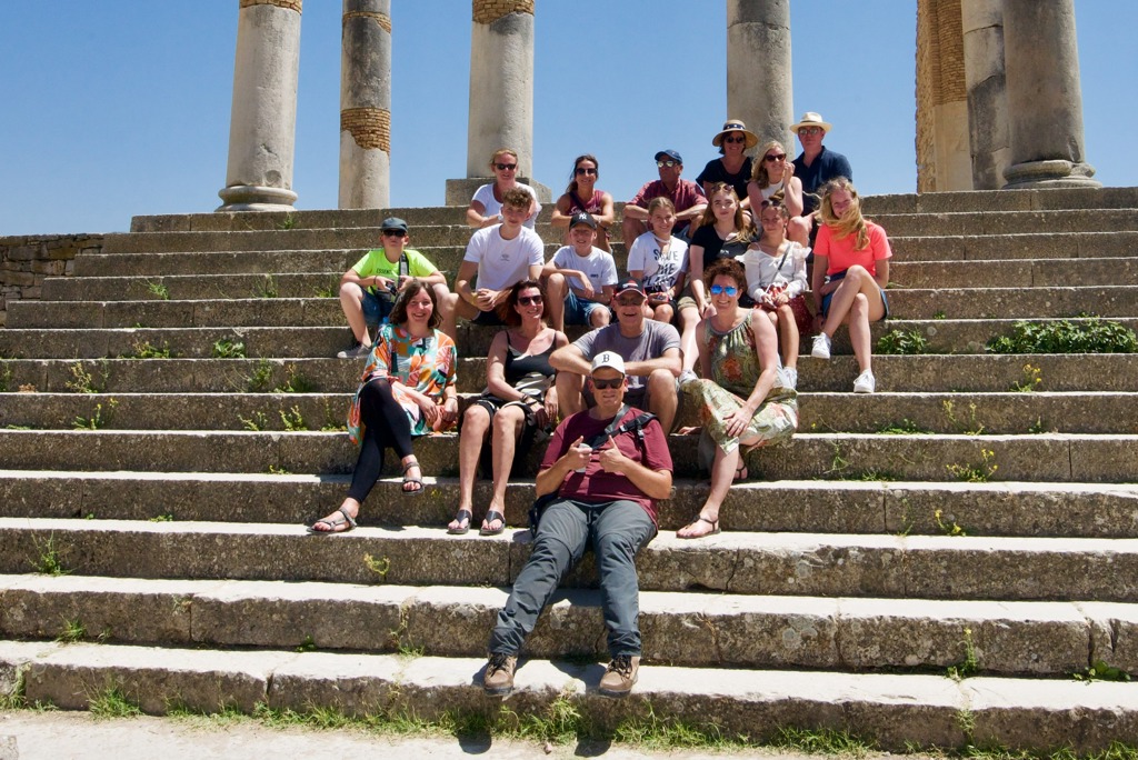 Reizigersgroep tijdens familiereis Marokko op stenen trappen bij Romeinse ruïnes met zuilen.