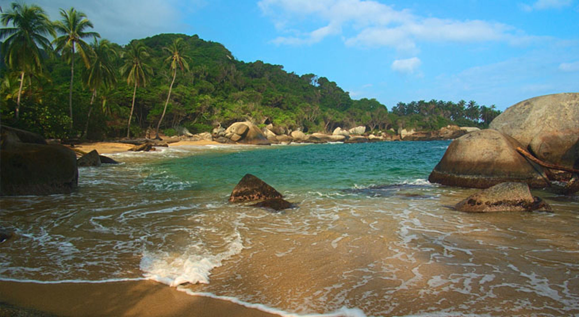 Tropisch strand in Colombia met palmbomen, granieten rotsen en helderblauw zeewater.