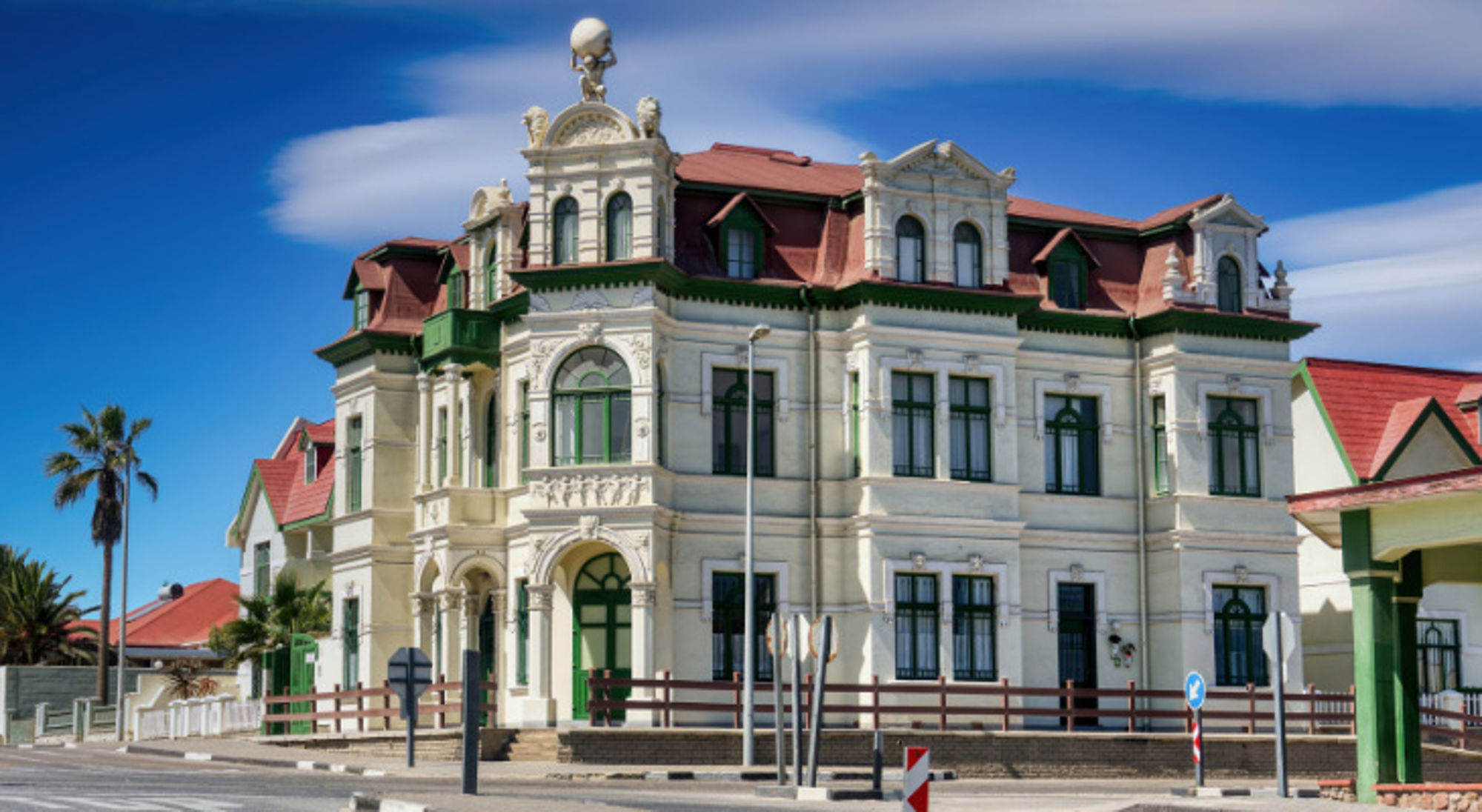 Historisch gebouw in Duitse koloniale stijl in Swakopmund, Namibië, met rood dak en groene kozijnen.