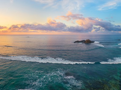 Zonsondergang boven de kust van Lombok met turquoise zee, golven en wit zandstrand.