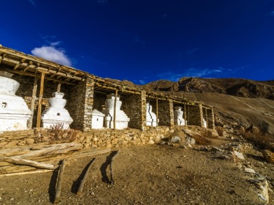Witte boeddhistische stupa’s langs een stenen klooster in het berglandschap van Spiti & Ladakh, onder een blauwe lucht.