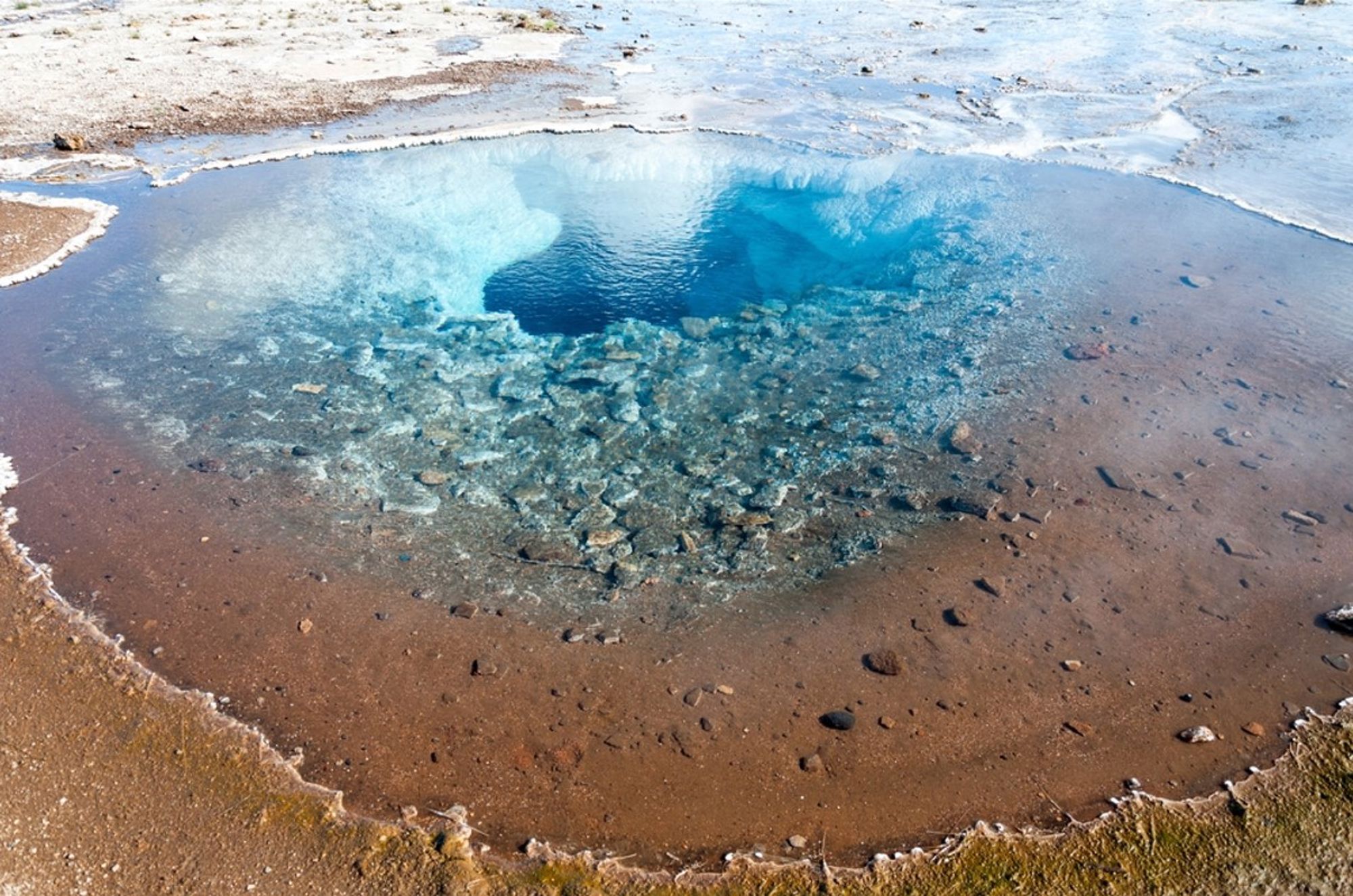 Helderblauwe geothermische bron in IJsland, omringd door modder en mineraalafzettingen.