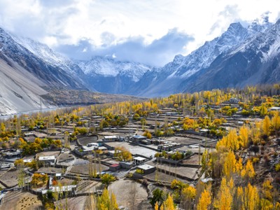 Herfstlandschap in de Hunza-vallei, Pakistan, met dorp tussen goudgele bomen en besneeuwde bergen.