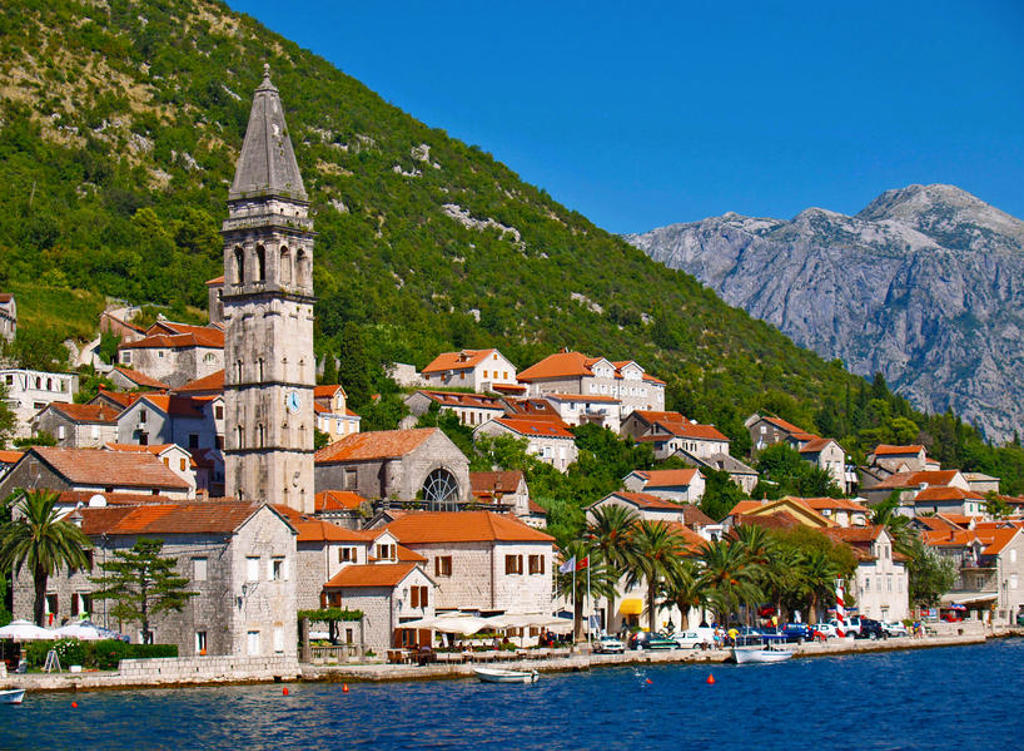 Perast aan de Baai van Kotor in Montenegro, met kerktoren, rode daken en bergen op de achtergrond.