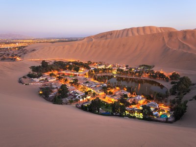 Oase Huacachina bij Ica met verlichte huizen rond lagune, omringd door hoge zandduinen in Peru.