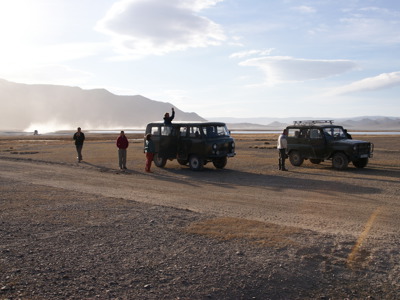Reizigers met busjes op een onverharde weg in de Mongoolse steppe, met bergen op de achtergrond.