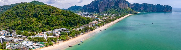 Panoramisch uitzicht op het strand van Ao Nang met turquoise zee, longtailboten en kalkstenen kliffen in Krabi, Thailand.