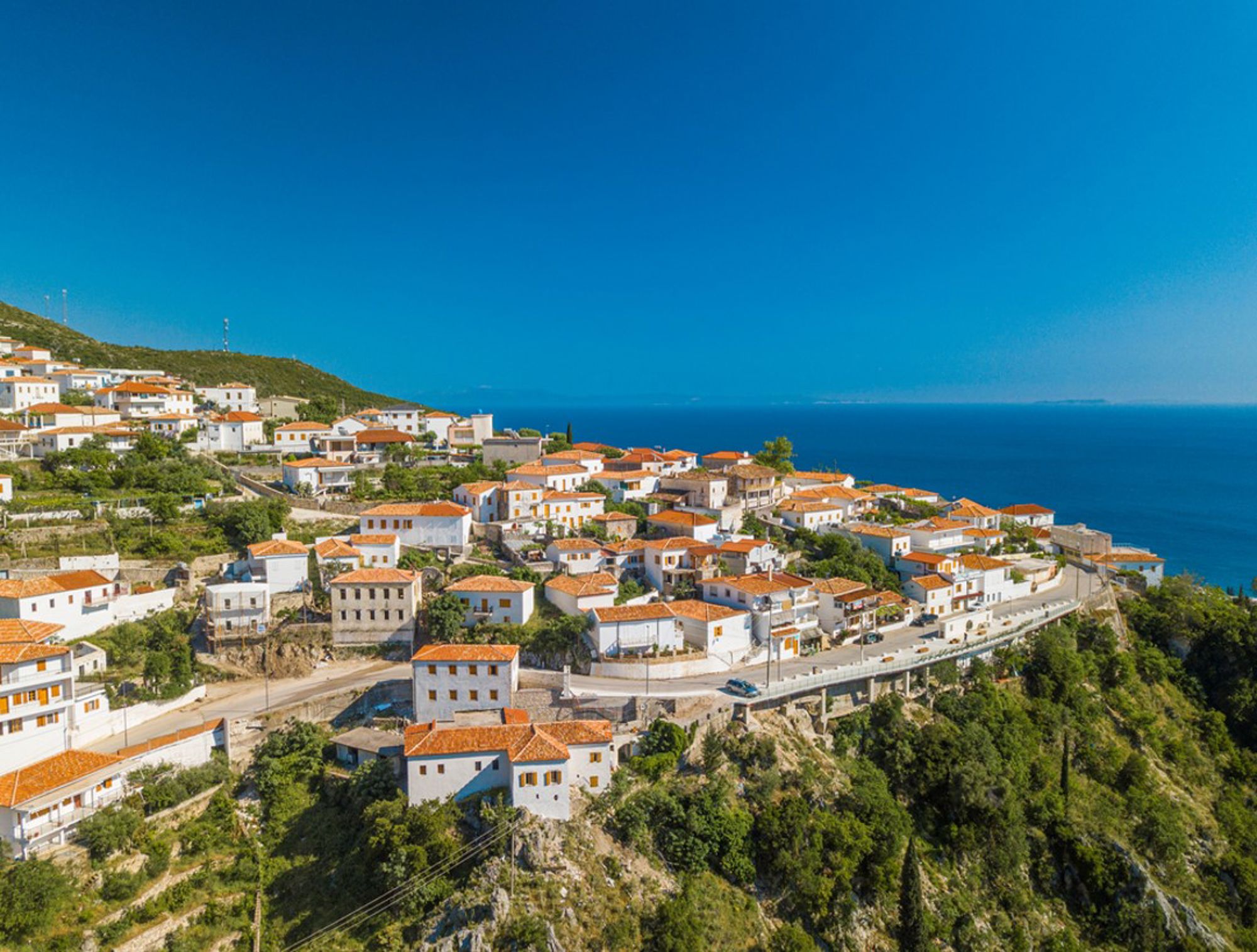 Panoramisch uitzicht op het kustdorp Dhërmi in Albanië, met witte huizen en rode daken boven de Ionische Zee.