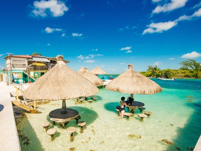 Rieten parasols en zitjes in ondiep turquoise water bij een strandbar in Belize, route Guatemala en Belize.