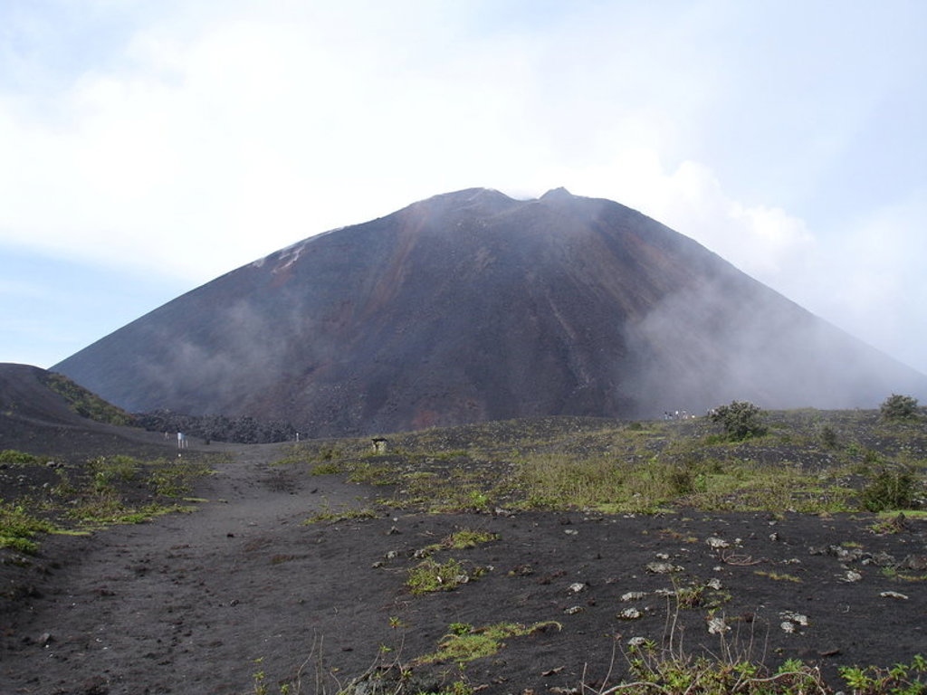 Vulkaanlandschap met zwarte lavagrond en een rokende vulkaankegel tijdens groepsrondreis Mexico, Guatemala en Honduras.