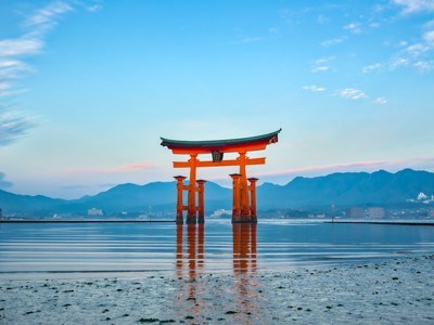 Oranje torii-poort in zee bij Miyajima, met bergen op de achtergrond tijdens zonsondergang.