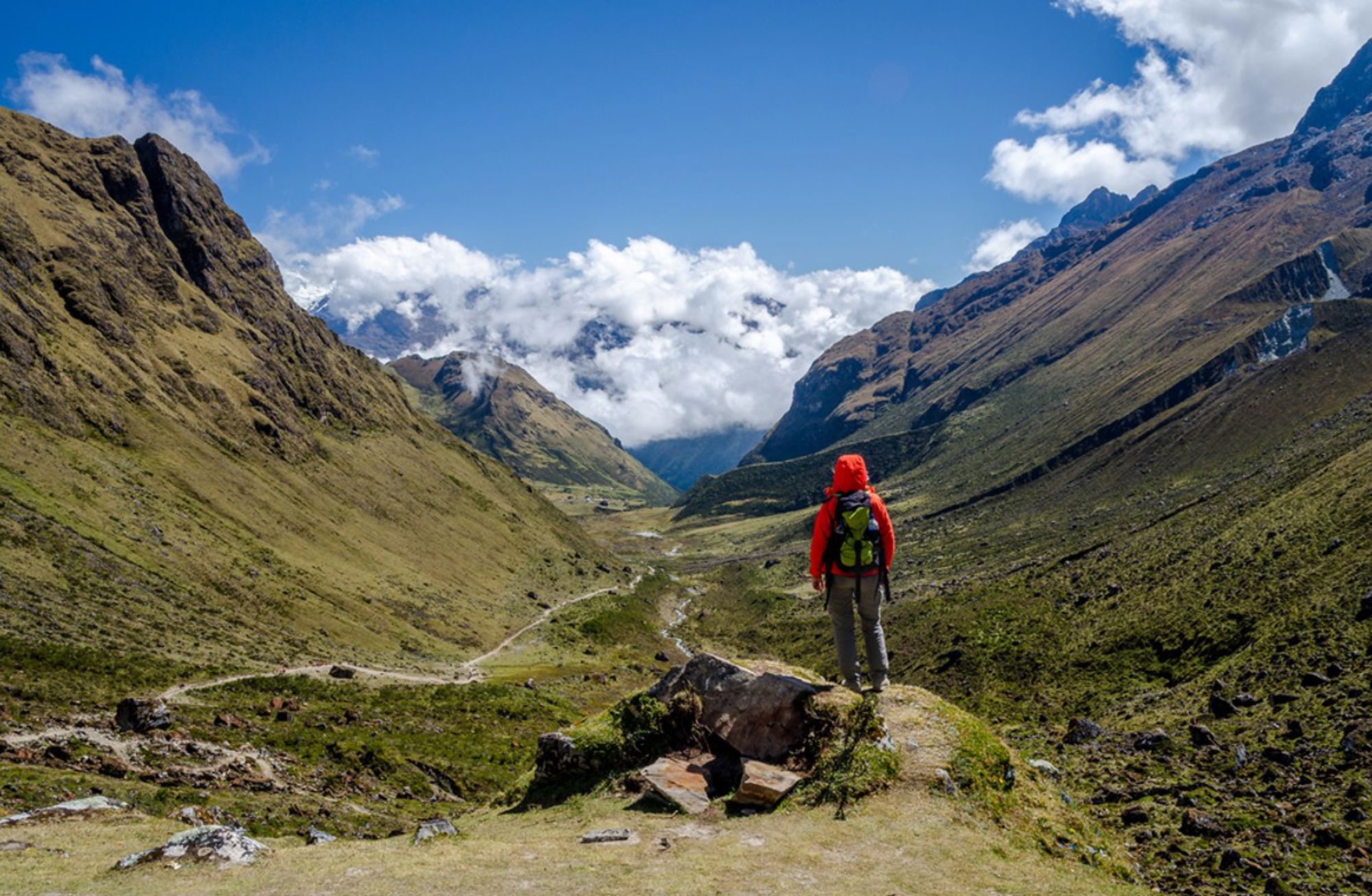 Wandelaar met rugzak kijkt uit over een bergvallei in de Peruaanse Andes onder een blauwe lucht.