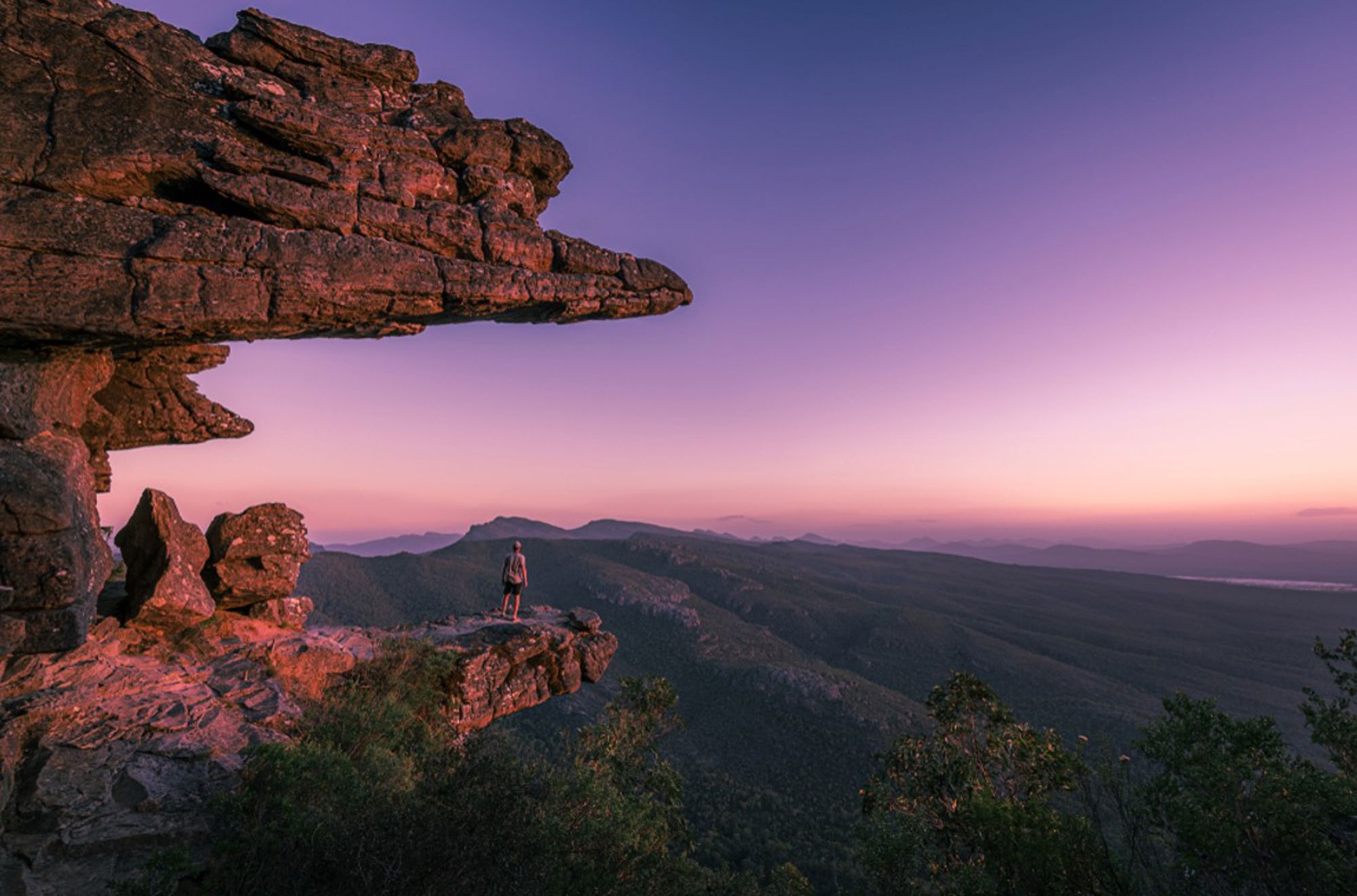 Uitzicht vanaf rotsklif in de Grampians, Australië, met wandelaar bij zonsondergang.
