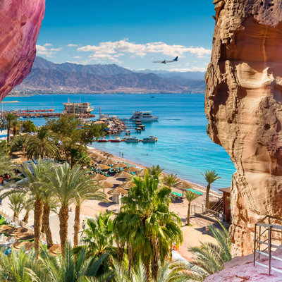Uitzicht op Aqaba aan de Rode Zee in Jordanië, met strand, palmbomen en bergen op de achtergrond.