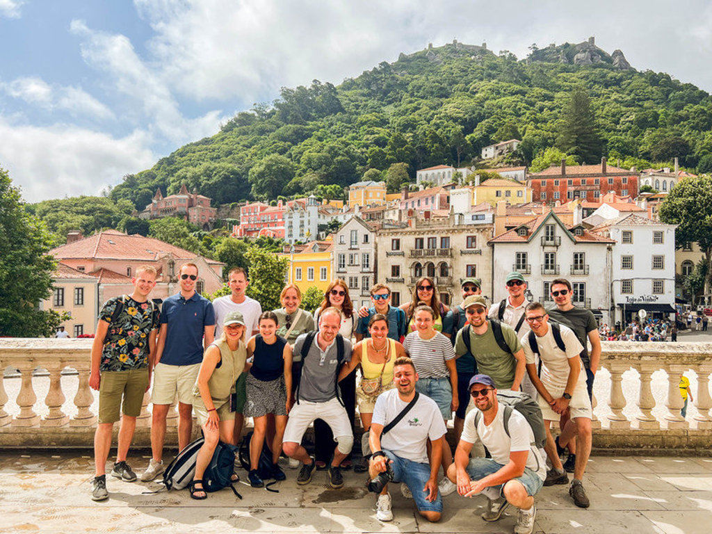 Groep 22-35ers reizigers in Sintra, Portugal, met kleurrijke huizen en groene heuvels op de achtergrond.