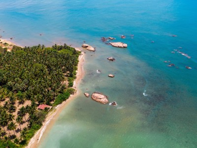 Palmenstrand aan de kust van Sri Lanka met rotsen in zee en helderblauw water.
