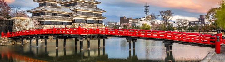 Matsumoto Castle met rode brug en weerspiegeling in de gracht bij zonsondergang.