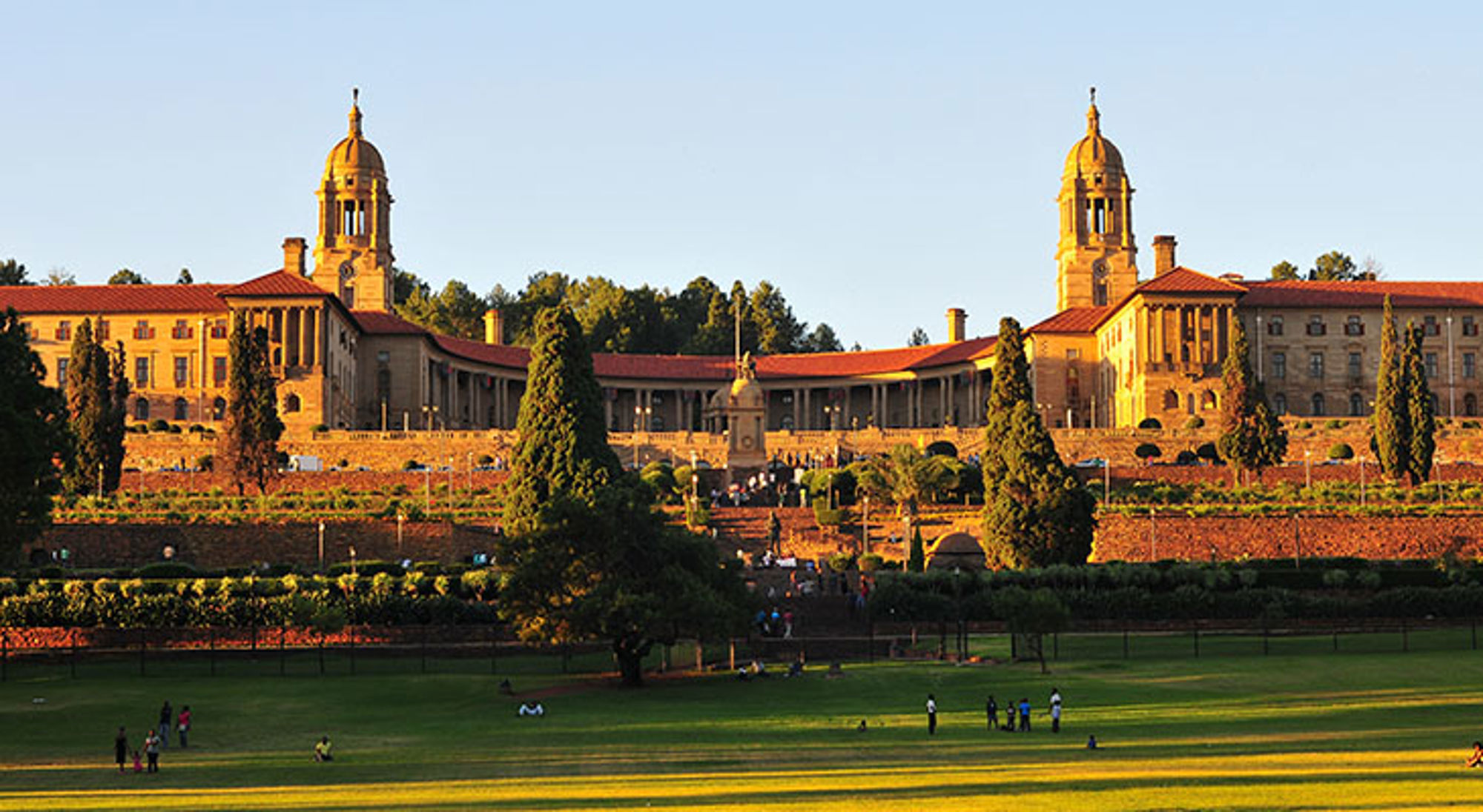 Het Uniegebouw in Pretoria Union Buildings in Pretoria, Zuid-Afrika, met tuinen en gazon in de voorgrond bij zonsondergang.
