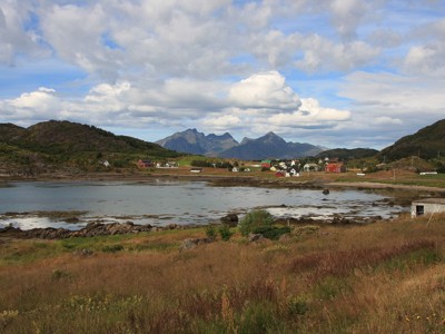Landschap op de Lofoten in Noorwegen met fjord, kleurrijk dorp en bergen onder een bewolkte lucht.