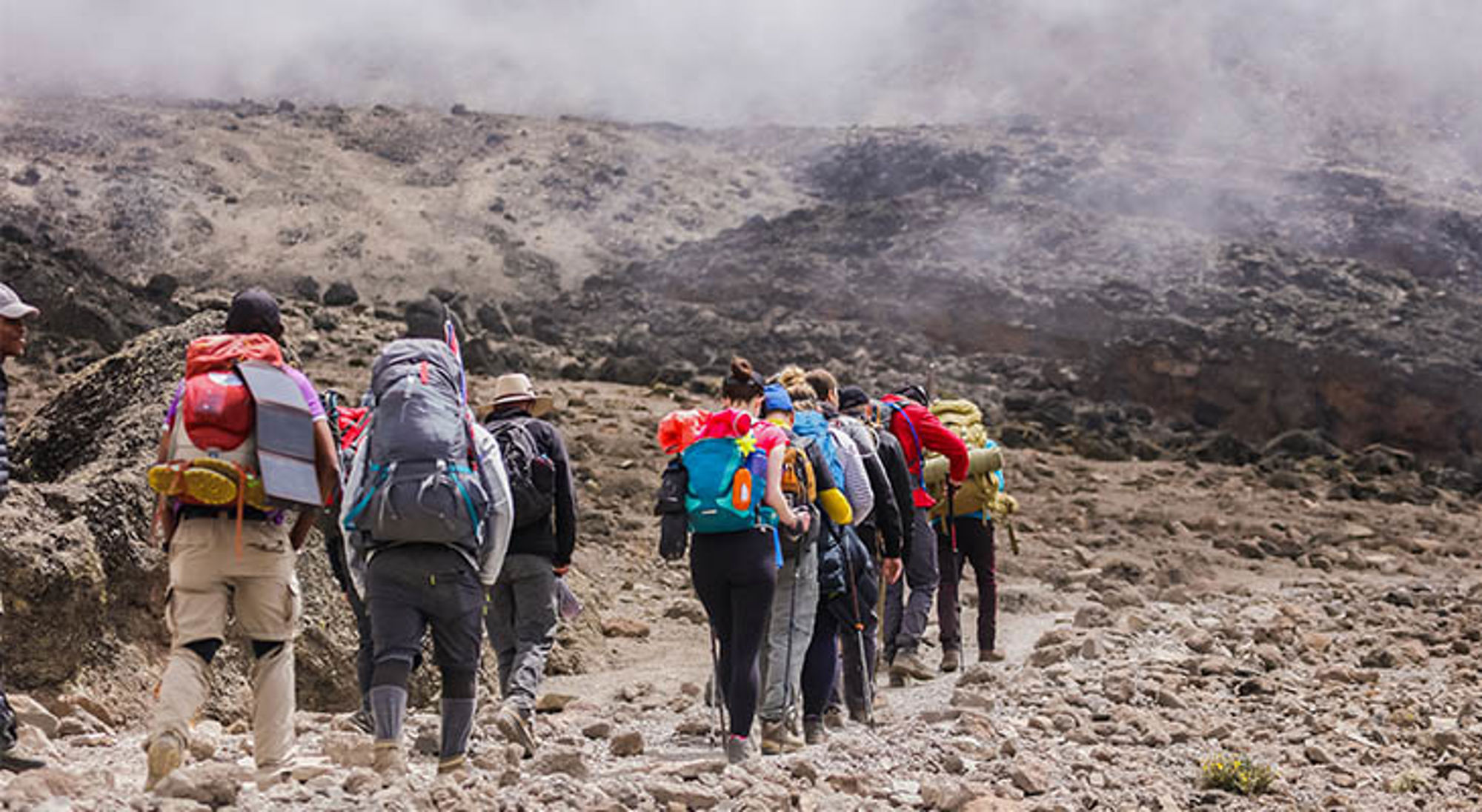 Wandelaars en bergbeklimmers op Kilimanjaro Groep wandelaars met rugzakken op een rotsachtig bergpad tijdens een trekking in Tanzania.