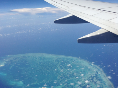 Vleugel van een vliegtuig boven de Caribische Zee met een tropisch eiland en turquoise lagune, Route Mexico.