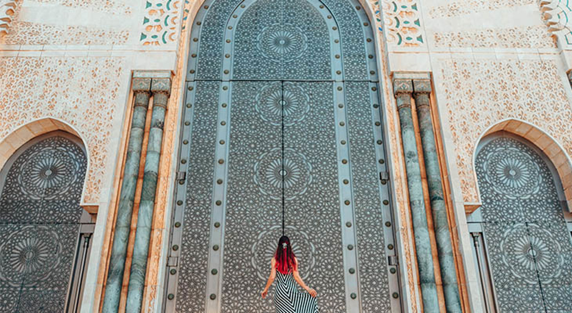 Vrouw voor imposante, rijk versierde poort van de Hassan II-moskee in Casablanca, Marokko.